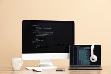 Photo of Programmer's workplace. Modern computer with unfinished code, laptop and other supplies on desk