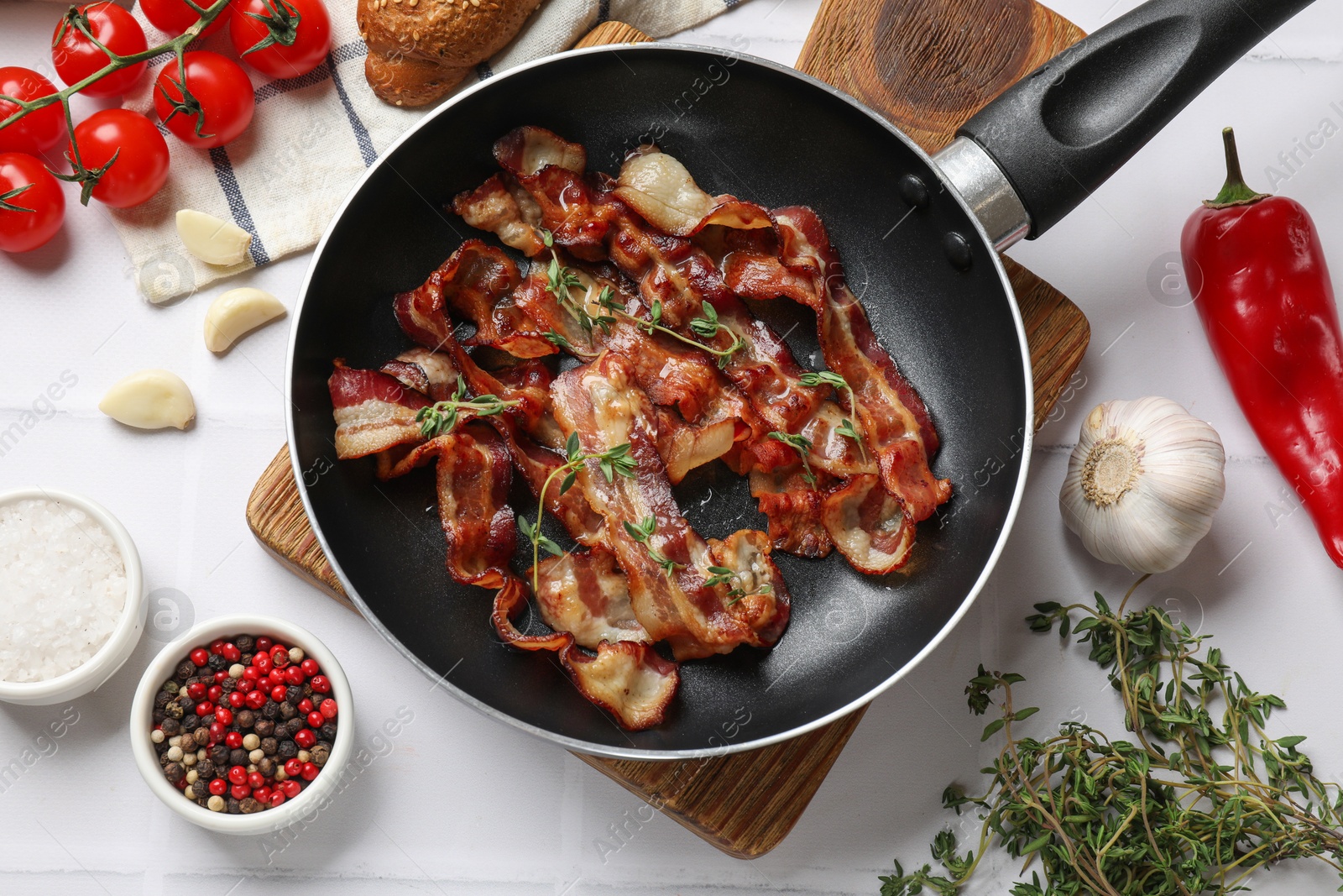 Photo of Delicious bacon slices in frying pan and products on white tiled table, flat lay