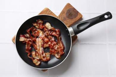 Photo of Delicious bacon slices in frying pan on white tiled table, top view