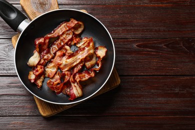 Photo of Delicious bacon slices in frying pan on wooden table, top view. Space for text