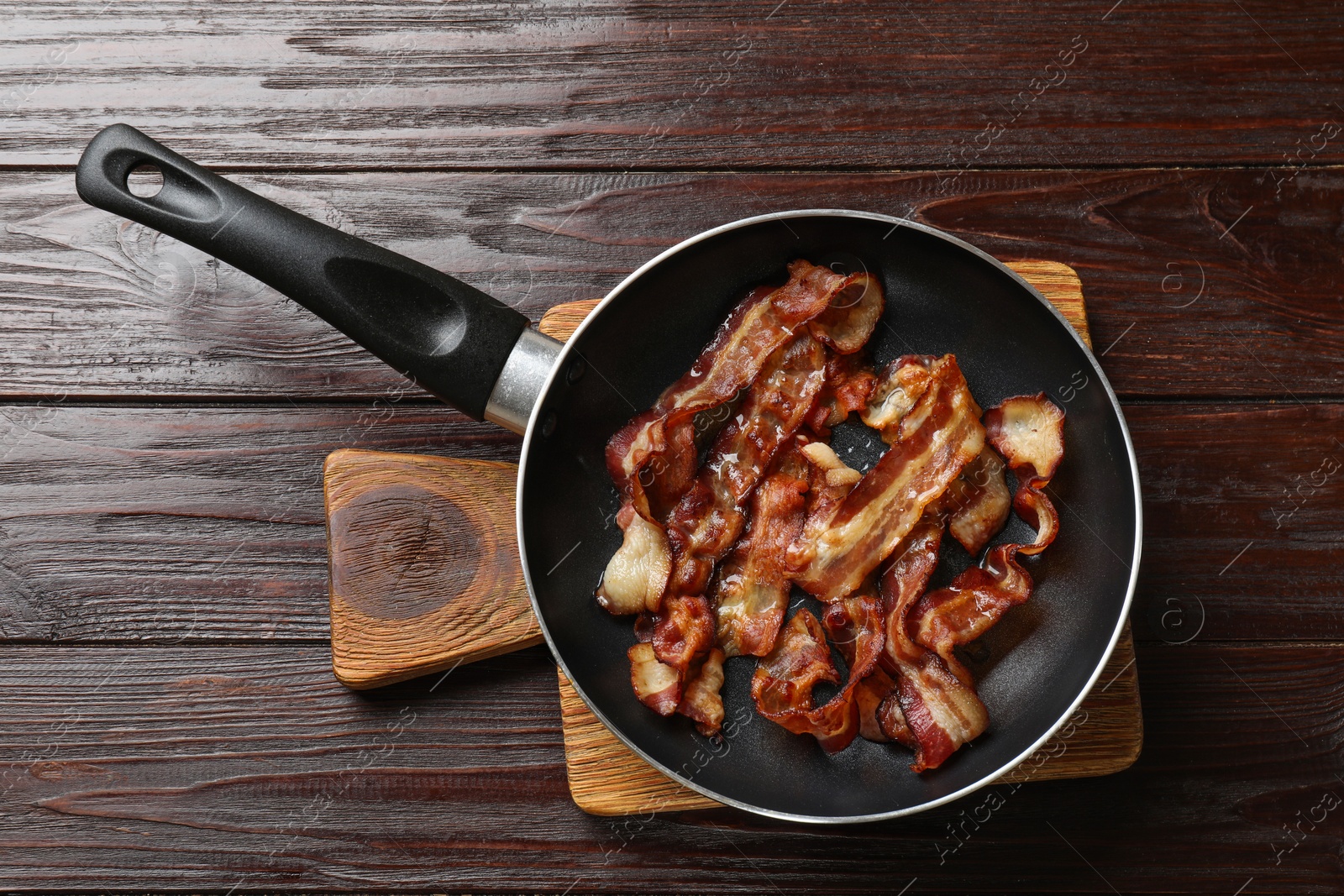 Photo of Delicious bacon slices in frying pan on wooden table, top view