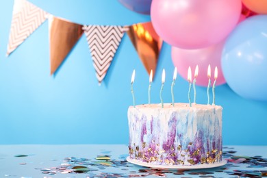 Photo of Tasty Birthday cake with burning candles and party decor on light blue background. Space for text