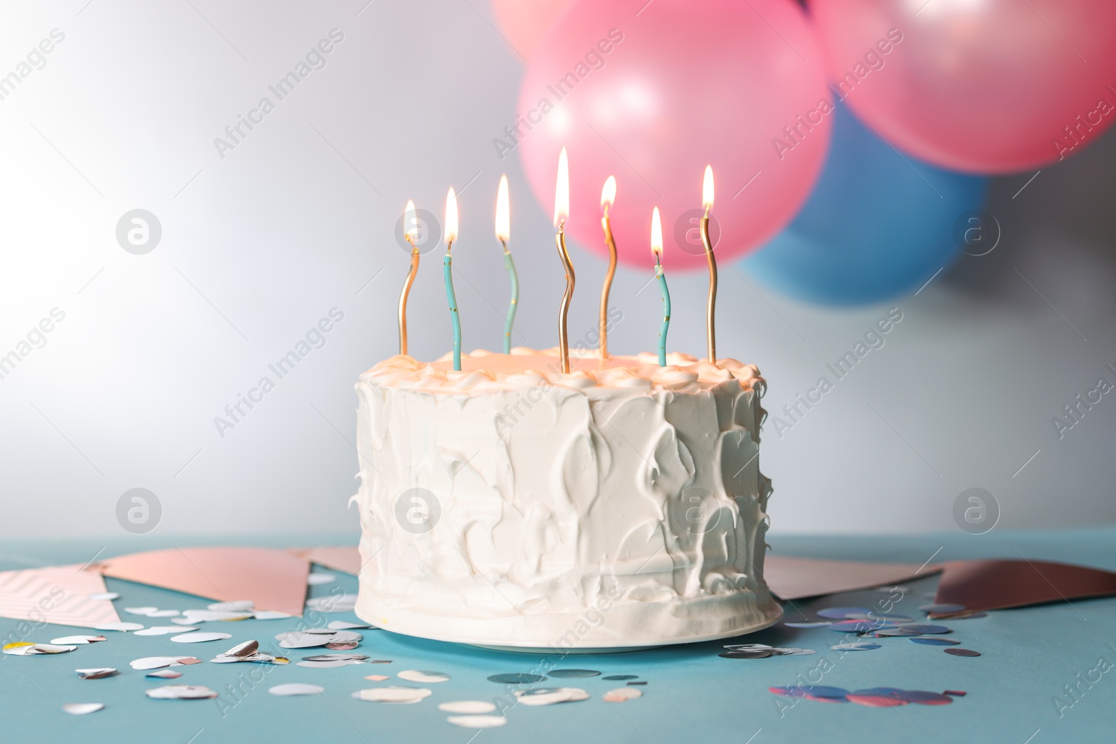 Photo of Tasty Birthday cake with burning candles and party decor on light blue table against gray background