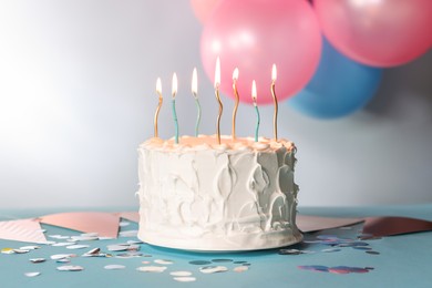 Photo of Tasty Birthday cake with burning candles and party decor on light blue table against gray background