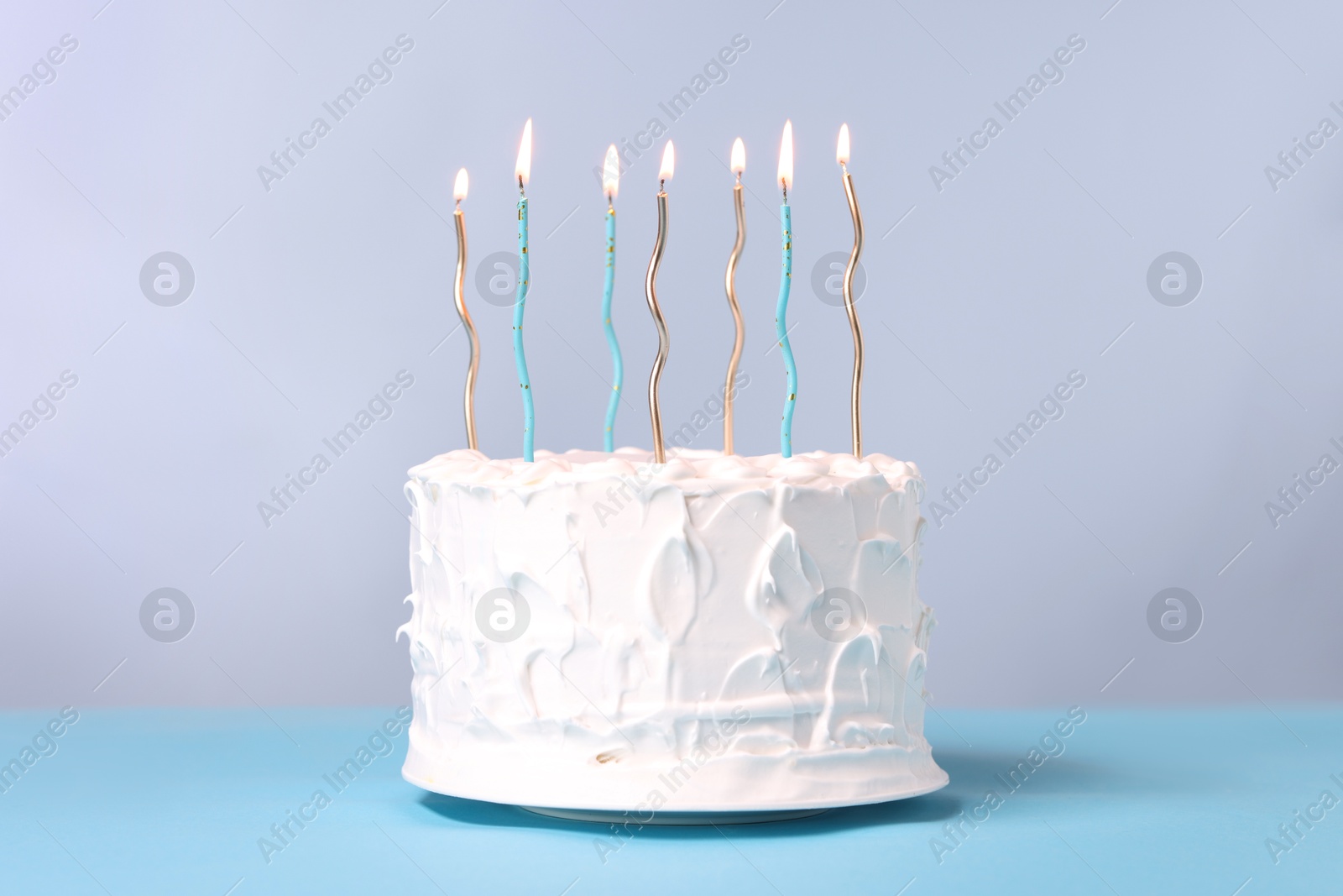 Photo of Tasty Birthday cake with burning candles on light blue table against gray background