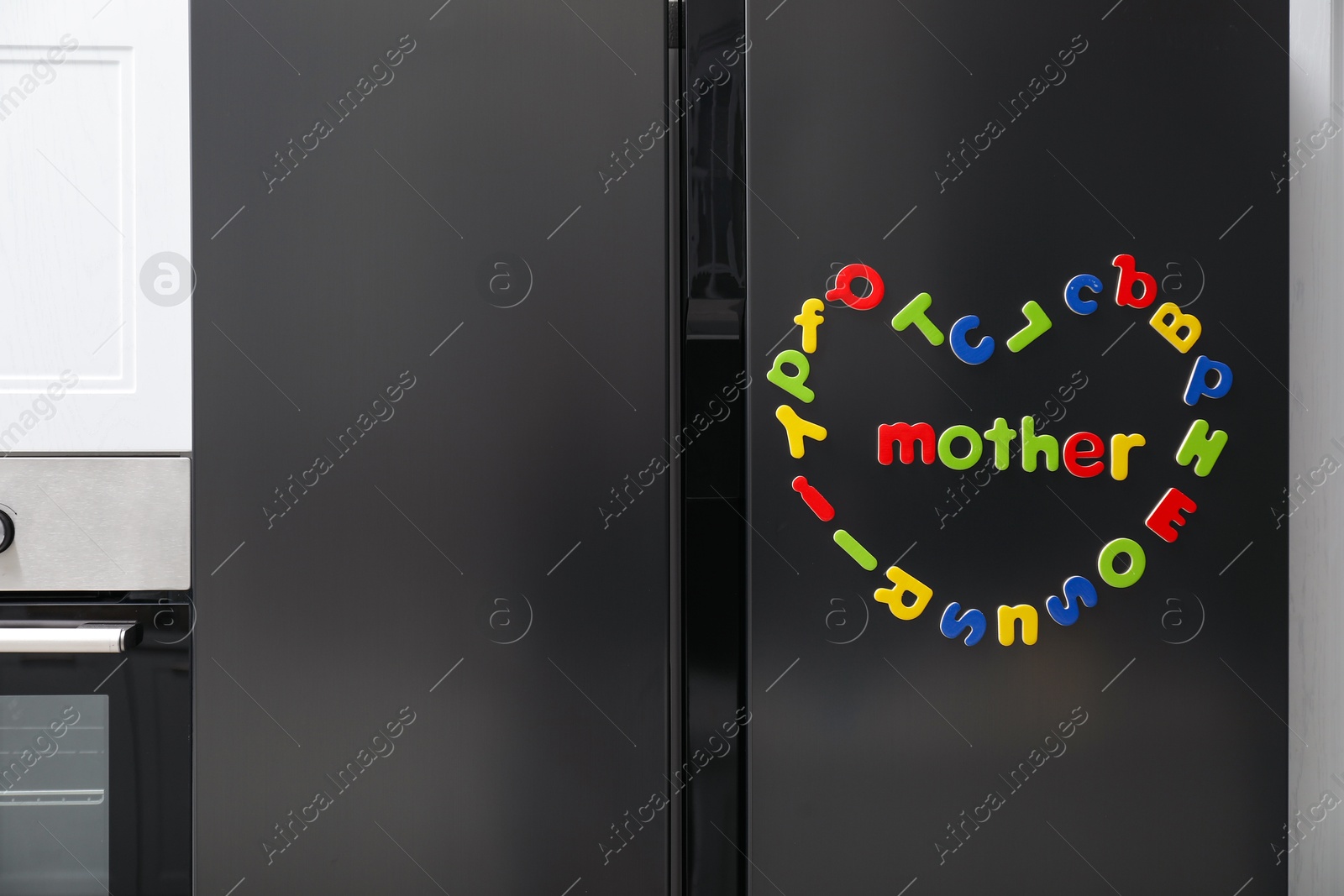 Photo of Word Mother and heart made of many bright magnetic letters on fridge indoors. Learning alphabet