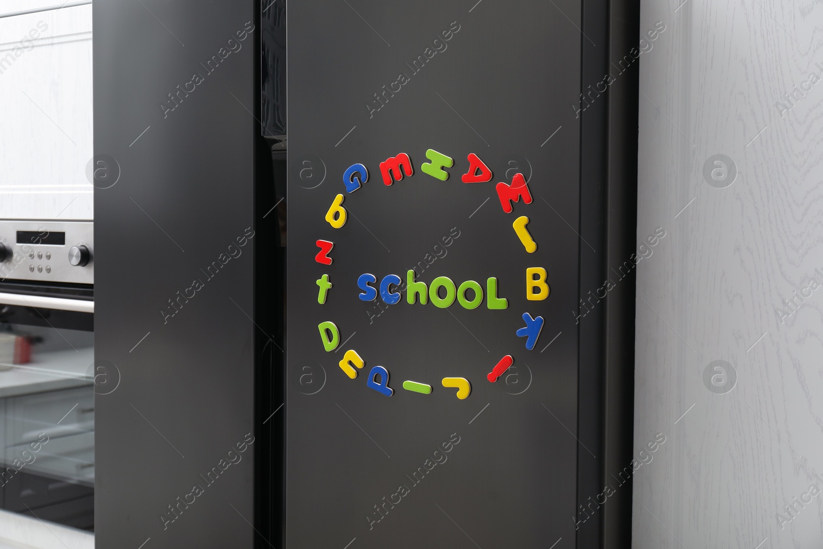 Photo of Word School and circle made of many bright magnetic letters on fridge indoors. Learning alphabet