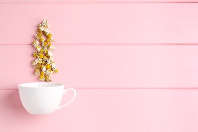 Photo of Chamomile flowers and white cup on pink wooden table, top view. Space for text