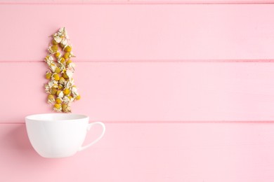 Chamomile flowers and white cup on pink wooden table, top view. Space for text