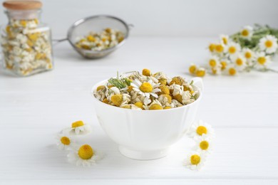 Photo of Dry and fresh chamomile flowers in bowl on white wooden table