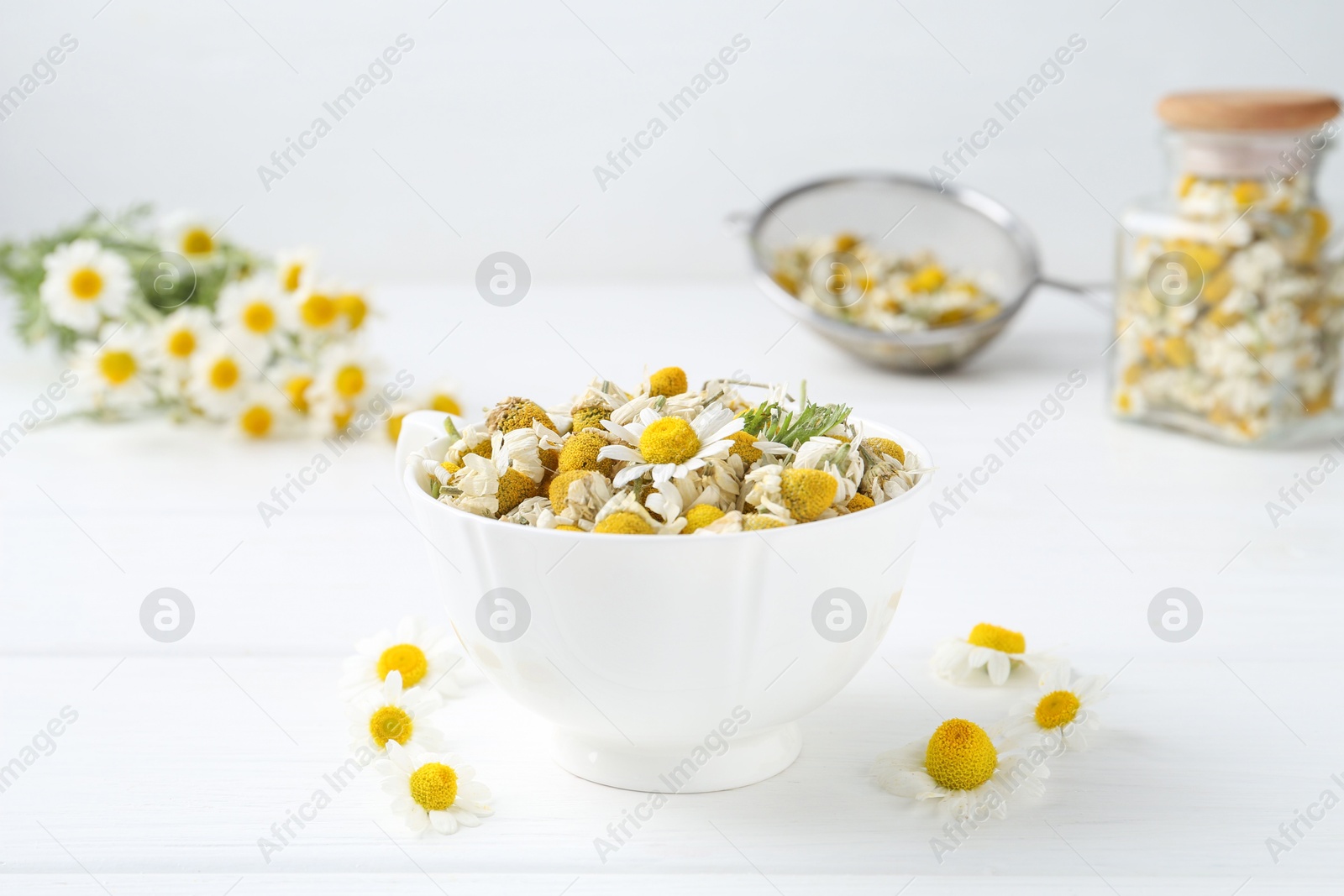 Photo of Dry and fresh chamomile flowers in bowl on white wooden table