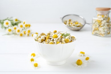 Photo of Dry and fresh chamomile flowers in bowl on white wooden table