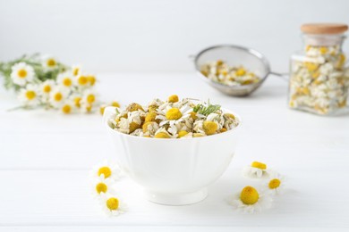 Dry and fresh chamomile flowers in bowl on white wooden table