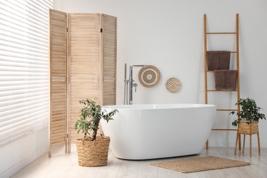 Photo of Wooden folding screen, bathtub and green houseplants in bathroom