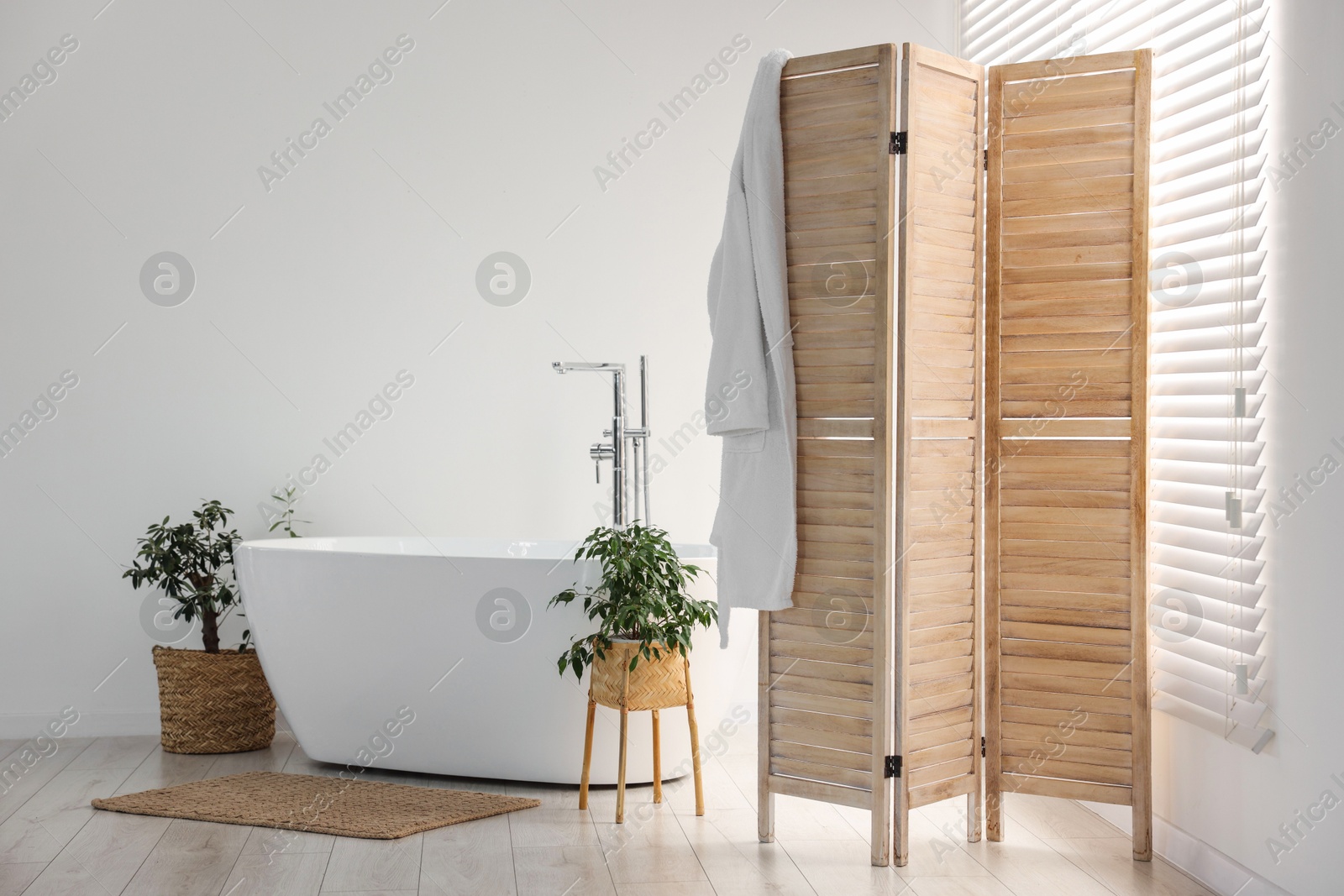 Photo of Wooden folding screen, bathtub and green houseplants in bathroom