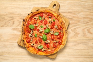 Delicious pizza with tomatoes, mushrooms and basil on wooden table, top view.