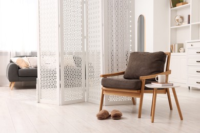 Photo of White folding screen, armchair and wooden table in living room