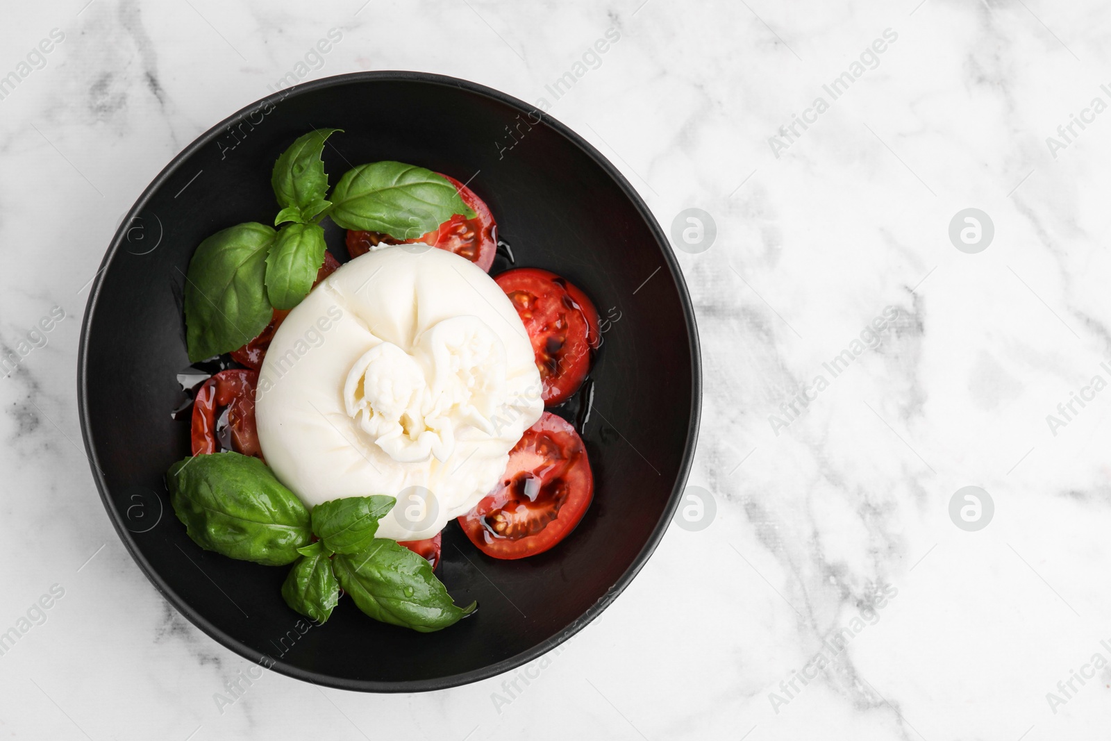 Photo of Delicious burrata cheese, tomatoes and basil in bowl on white marble table, top view. Space for text