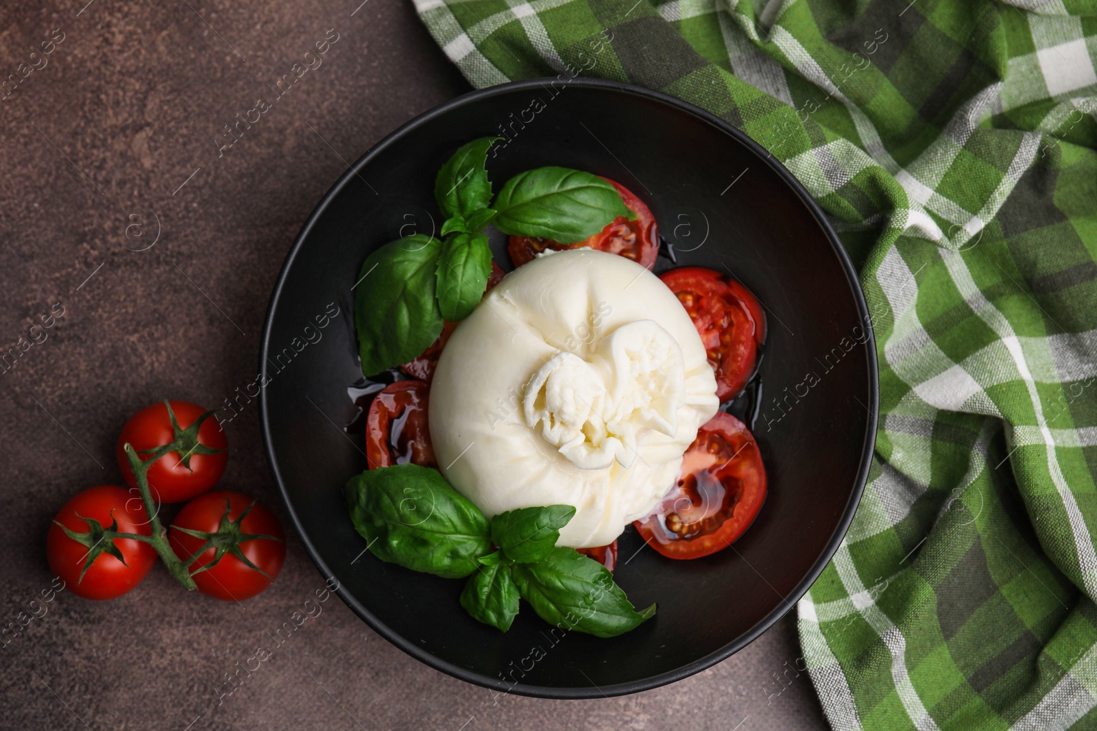 Photo of Delicious burrata cheese, tomatoes and basil in bowl on brown table, top view