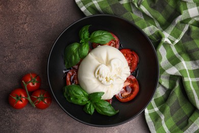 Photo of Delicious burrata cheese, tomatoes and basil in bowl on brown table, top view