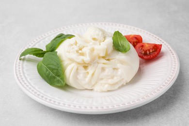 Photo of Delicious burrata cheese, tomatoes and basil on light table, closeup