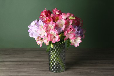 Photo of Beautiful alstroemeria flowers in vase on wooden table against green background