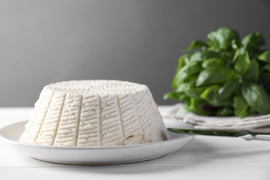 Photo of Tasty ricotta (cream cheese), knife and basil on white wooden table, closeup