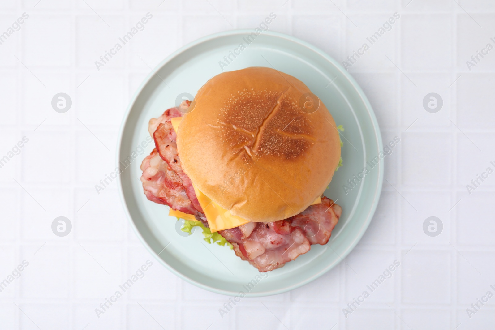 Photo of Delicious burger with bacon and cheese on white tiled table, top view