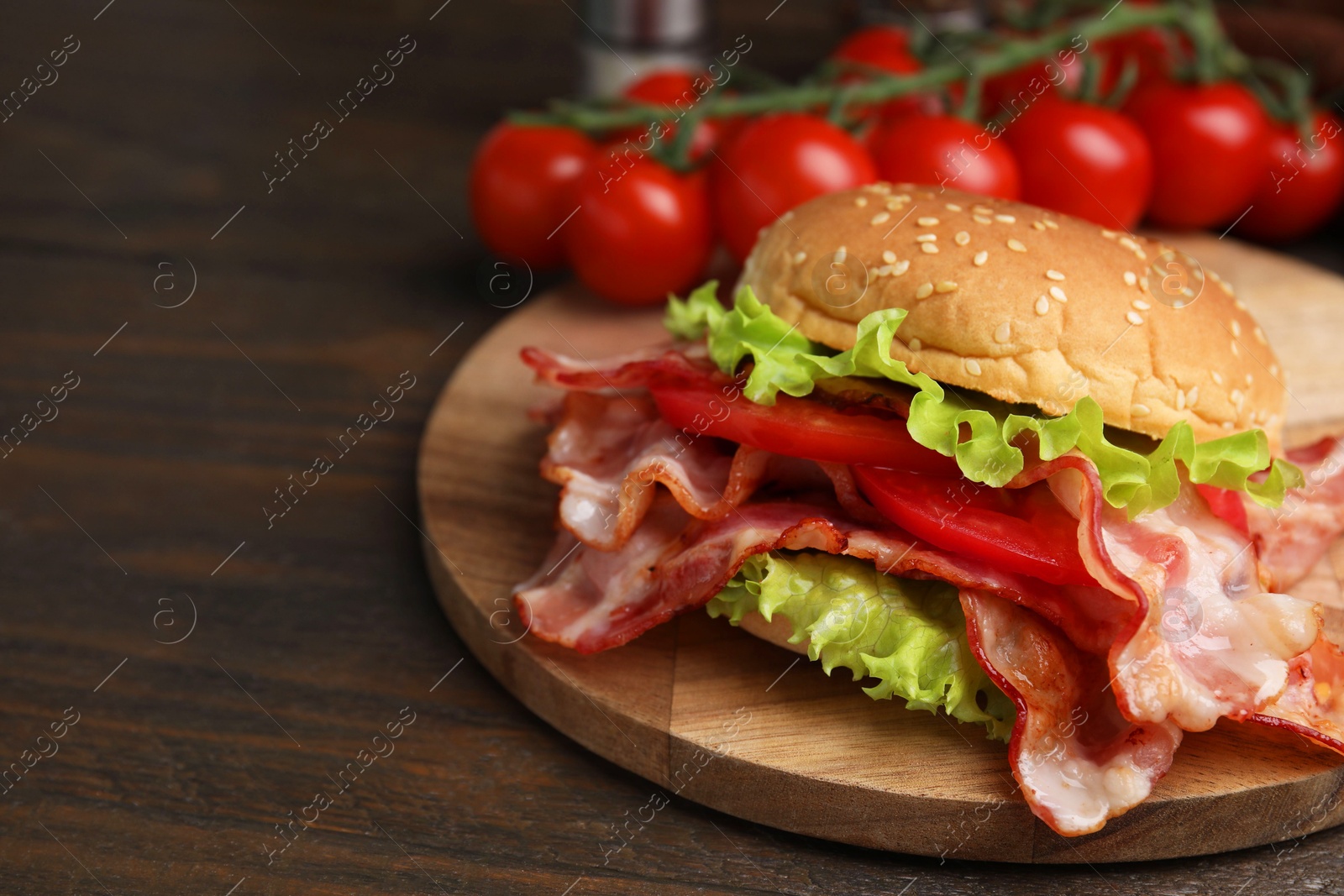 Photo of Delicious burger with bacon, tomato and lettuce on wooden table, space for text