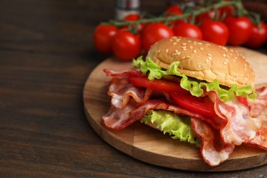 Delicious burger with bacon, tomato and lettuce on wooden table, space for text