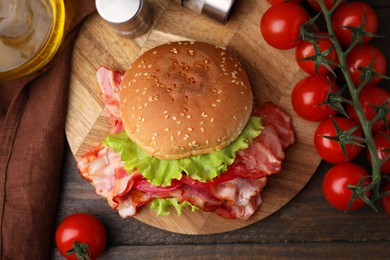 Delicious burger with bacon, tomatoes and lettuce on wooden table, top view