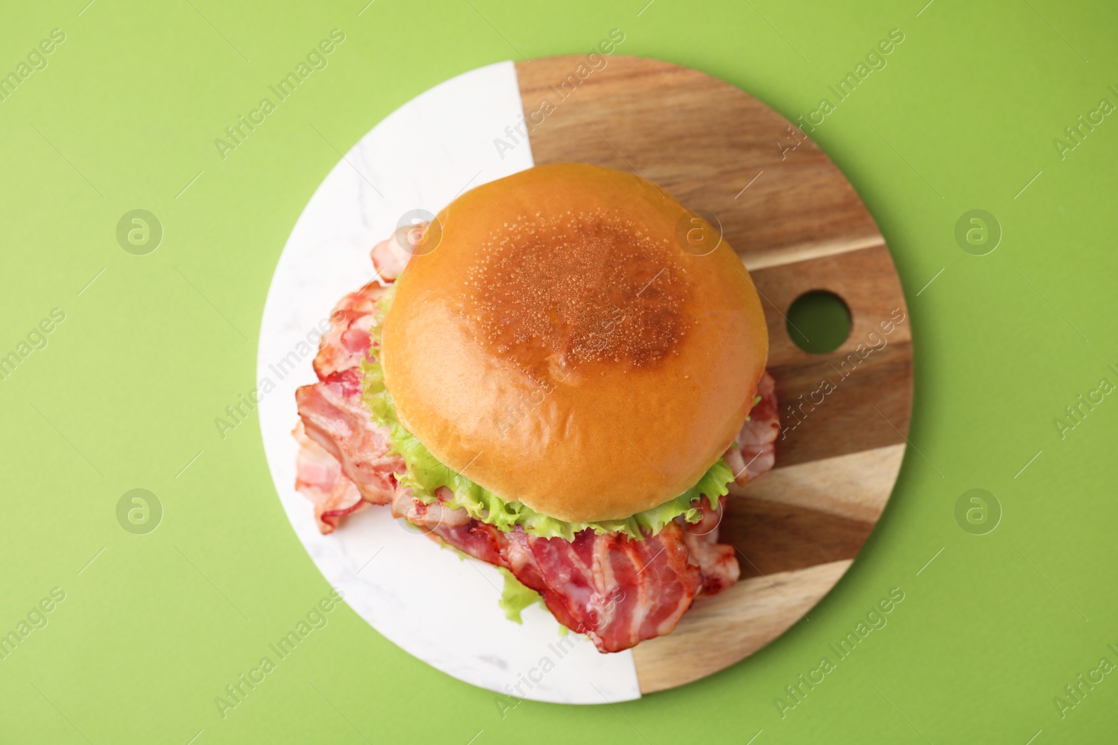 Photo of Delicious burger with bacon and lettuce on green background, top view