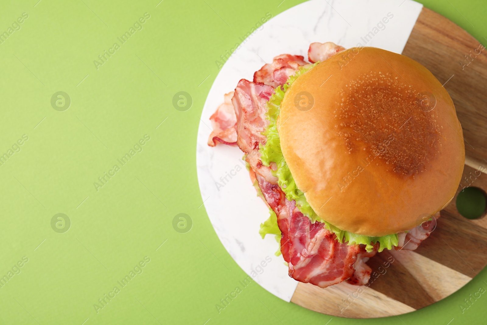 Photo of Delicious burger with bacon and lettuce on green background, top view. Space for text