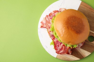 Photo of Delicious burger with bacon and lettuce on green background, top view. Space for text