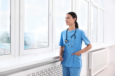 Photo of Smiling nurse with clipboard near window in clinic. Space for text