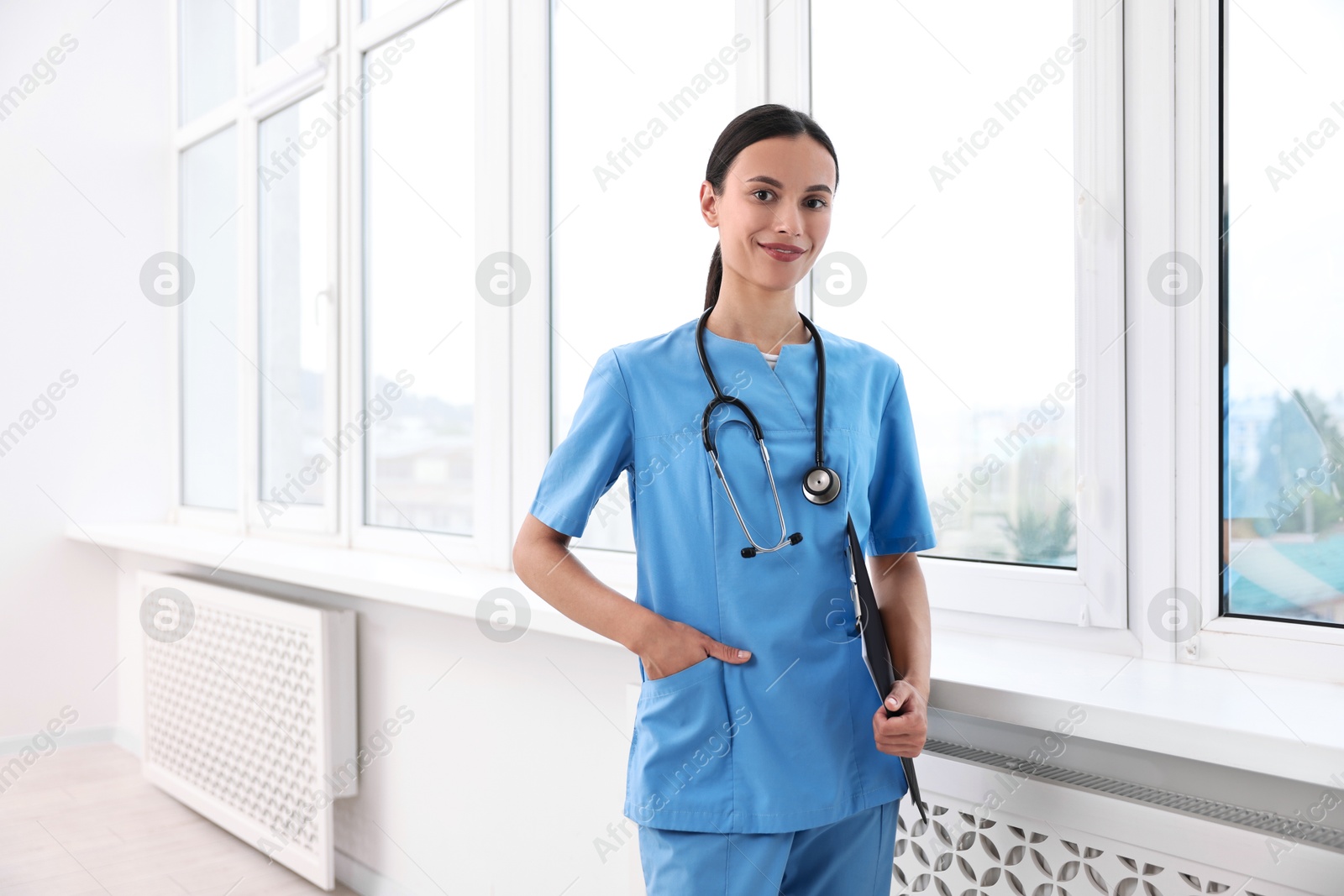 Photo of Beautiful nurse with clipboard near window in clinic. Space for text