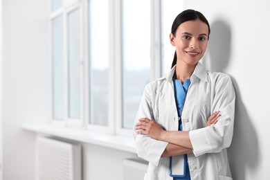 Photo of Smiling nurse with crossed arms near window in clinic. Space for text