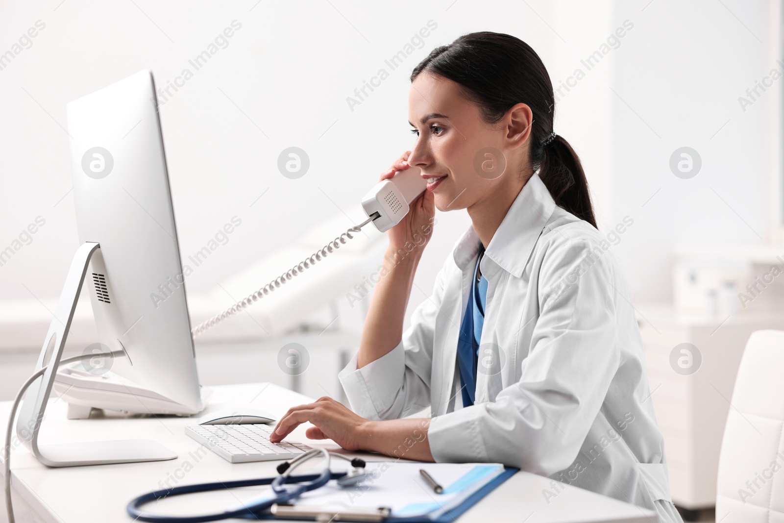 Photo of Smiling nurse consulting patient by phone at table in clinic