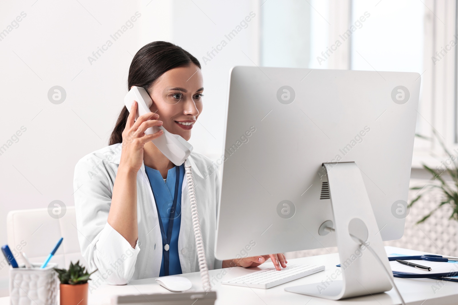 Photo of Smiling nurse consulting patient by phone at table in clinic