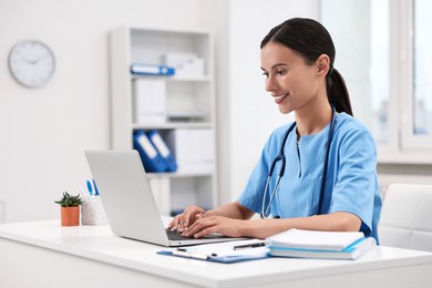 Photo of Smiling nurse working with laptop at table in clinic