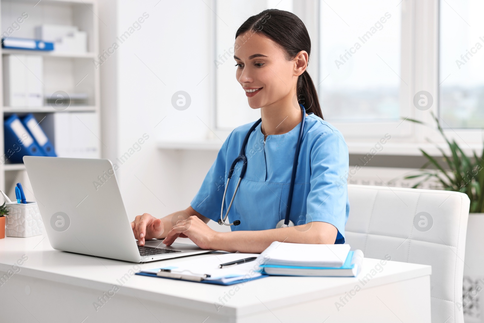 Photo of Smiling nurse working with laptop at table in clinic