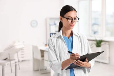 Beautiful nurse with clipboard writing notes in clinic. Space for text