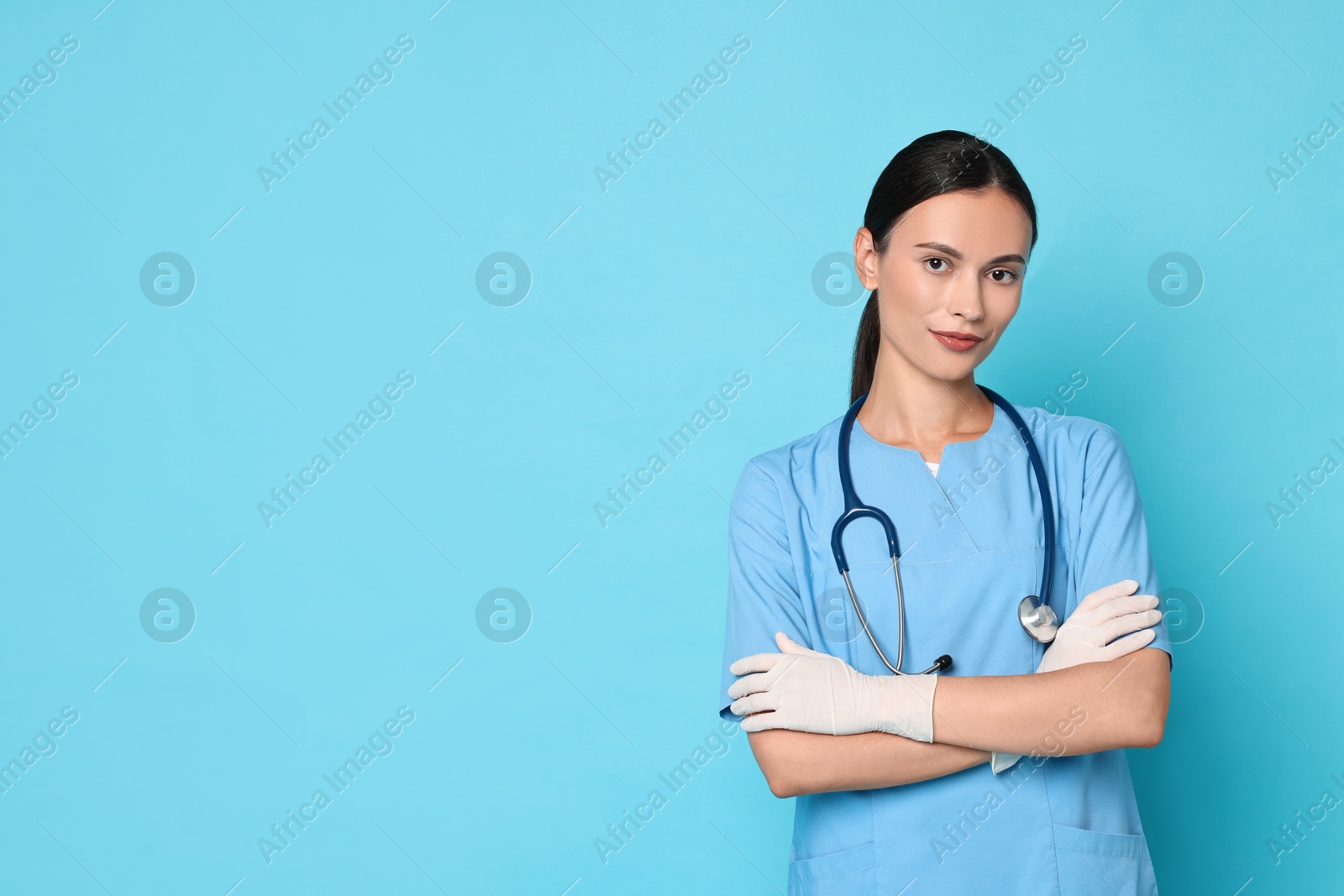 Photo of Beautiful nurse with crossed arms on light blue background. Space for text