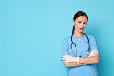 Photo of Beautiful nurse with crossed arms on light blue background. Space for text