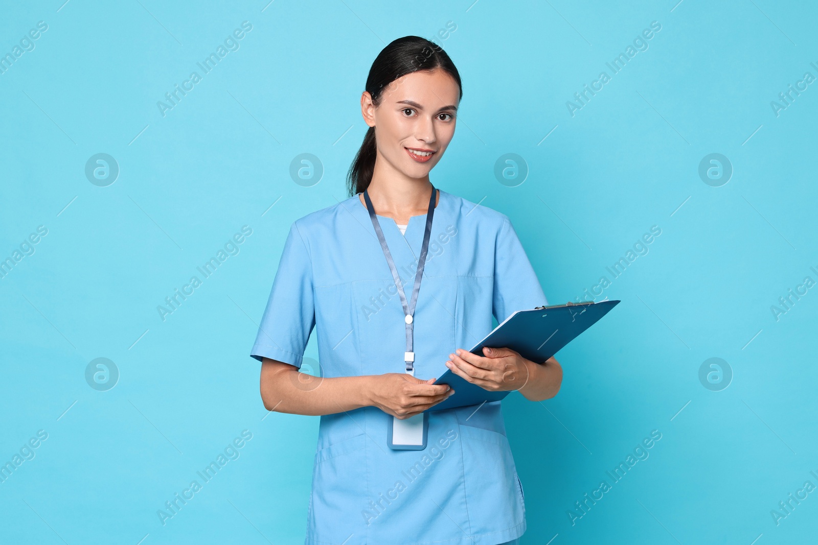 Photo of Smiling nurse with clipboard on light blue background