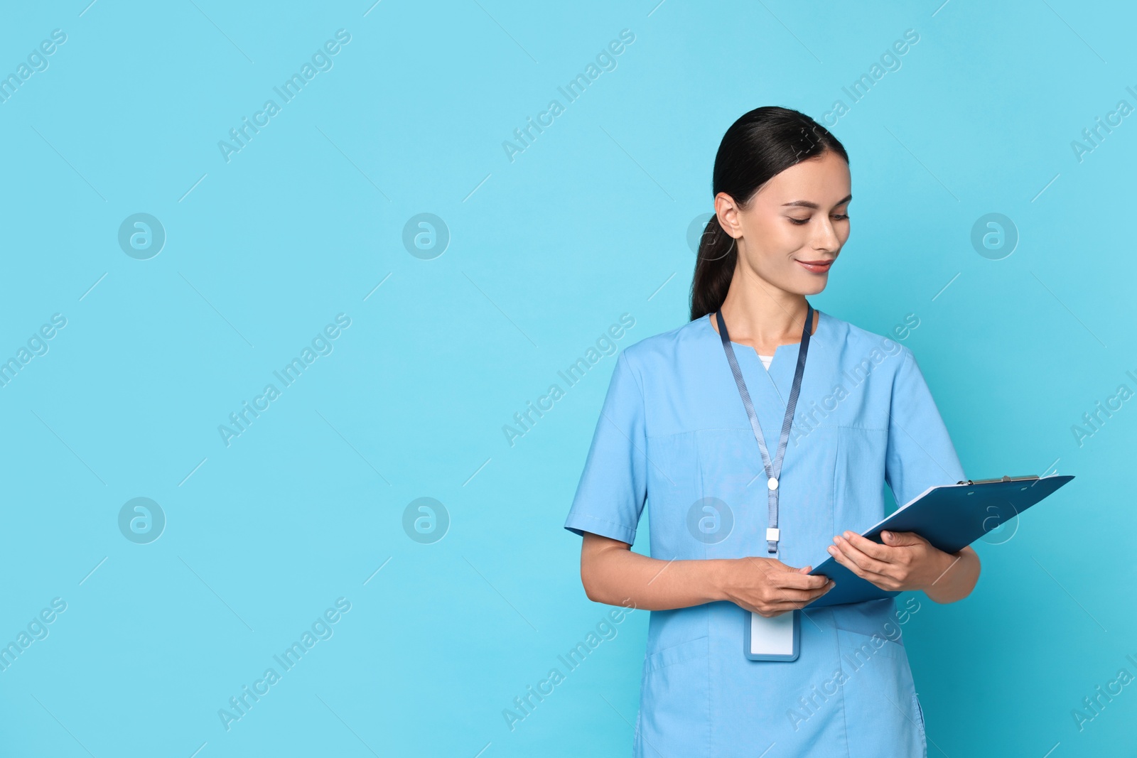 Photo of Beautiful nurse with clipboard on light blue background. Space for text