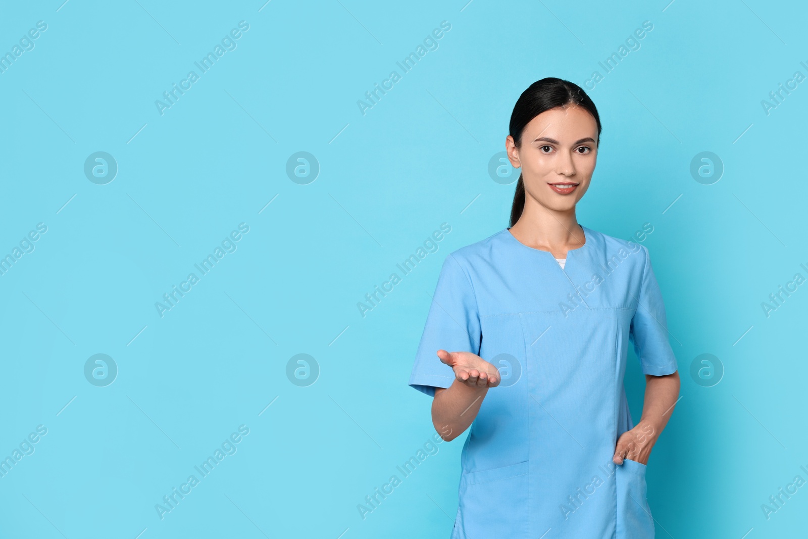 Photo of Smiling nurse holding something on light blue background. Space for text