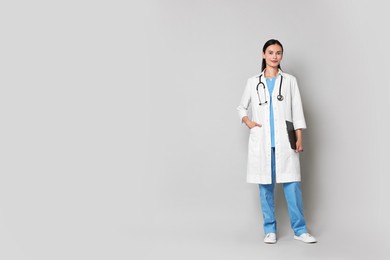 Beautiful nurse with clipboard on grey background. Space for text