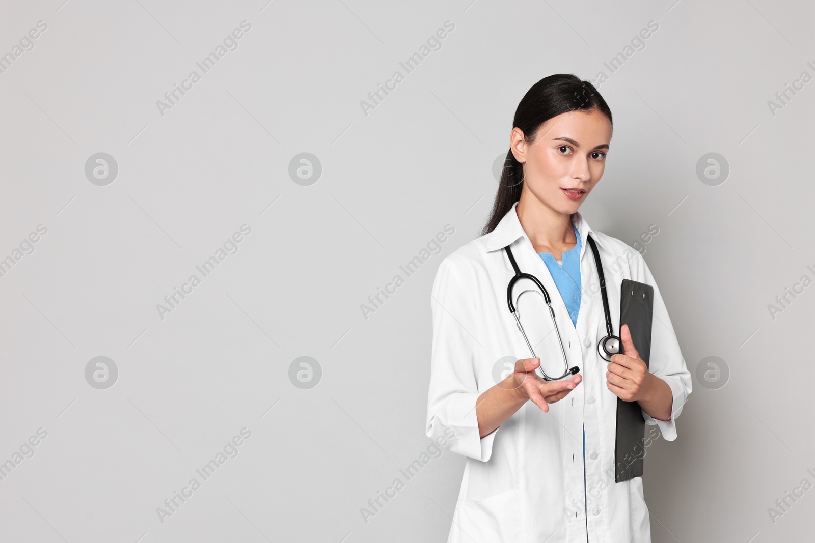 Photo of Beautiful nurse with clipboard holding something on grey background. Space for text