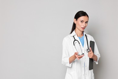 Beautiful nurse with clipboard holding something on grey background. Space for text